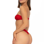 Side view of model wearing scarlet red bandeau Lola bikini top and matching Brazilian cut bikini bottom by Aventura Swimwear. 