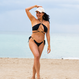 Woman in a black bikini and white cap standing on a beach with a clear sky.