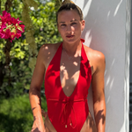 Woman in a red swimsuit standing outdoors with greenery and flowers in the background