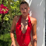 Woman in a red swimsuit standing outdoors with greenery and flowers in the background