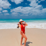 Woman in a red swimsuit standing on a beach with blue sky and ocean.