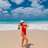 Woman in a red swimsuit standing on a beach with blue sky and ocean.