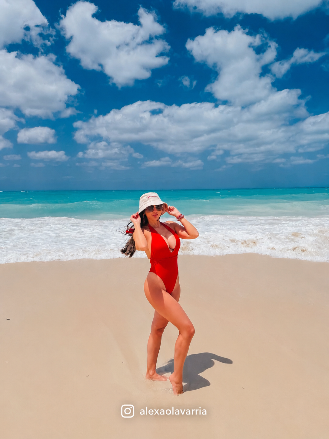 Woman in a red swimsuit standing on a beach with blue sky and ocean.