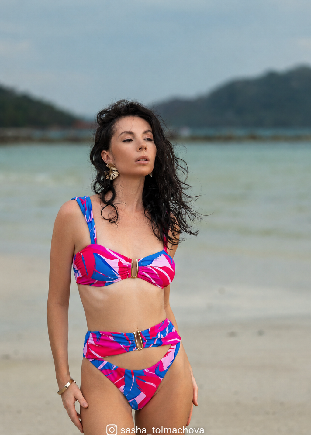 Woman in a colorful bikini standing on a beach with mountains in the background