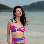 Woman in a colorful bikini standing on a beach with mountains in the background