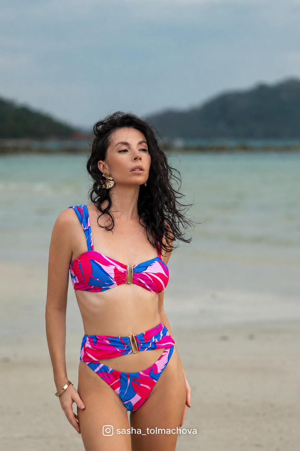 Woman in a colorful bikini standing on a beach with mountains in the background