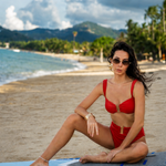 Woman in a red bikini sitting on a paddleboard at the beach with mountains in the background