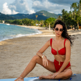 Woman in a red bikini sitting on a paddleboard at the beach with mountains in the background